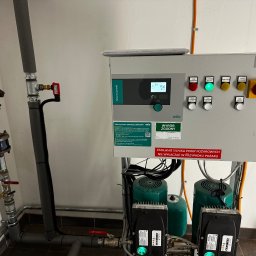 MK Electric System Marcin Kobrzyński - Panel sterowania Wilo SmartControl Fire 2x10A z zielonymi i czerwonymi diodami, podłączony do instalacji hydraulicznej z rurami i pompami. Widoczne napisy ostrzegawcze.