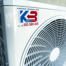 KLIMA-BROTHERS PIOTR ŚLIWKA - Biała jednostka zewnętrzna klimatyzacji z logo firmy 'Klima Brothers' i numerem telefonu. Widoczne elementy wentylatora i obudowy. Specjaliści od komfortu.
