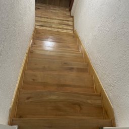 Perfect Wall - Drewniane schody z jasnego drewna, widok z góry, ściany z fakturą, podłoga wykończona panelami. Detal wykończenia wnętrza.