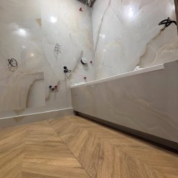 Exstra remont - Nowoczesna łazienka w trakcie wykańczania: marmurowe płytki ścienne, drewnopodobna podłoga ułożona w jodełkę, widoczne instalacje przed montażem armatury.