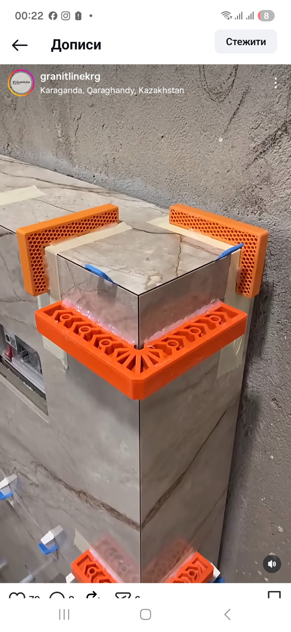 Układanie płytek na narożniku z użyciem pomarańczowych elementów poziomujących. Widoczna zaprawa i fragment ściany. Płytki w odcieniach szarości z delikatnym wzorem.