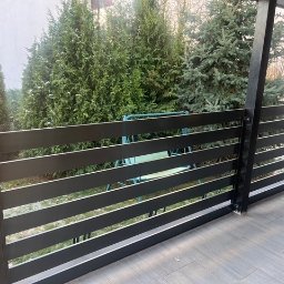 HUSSEG SPÓŁKA Z OGRANICZONĄ ODPOWIEDZIALNOŚCIĄ - Nowoczesna, pozioma balustrada metalowa w kolorze antracytowym, z widokiem na zielony ogród i huśtawkę. Minimalistyczny design, proste linie, szara podłoga z płytek.