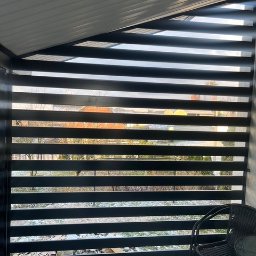 HUSSEG SPÓŁKA Z OGRANICZONĄ ODPOWIEDZIALNOŚCIĄ - Nowoczesna, pozioma, czarna osłona balkonu z widokiem na ogród. Minimalistyczny design z równomiernymi przerwami między lamelami. W tle widoczny budynek.