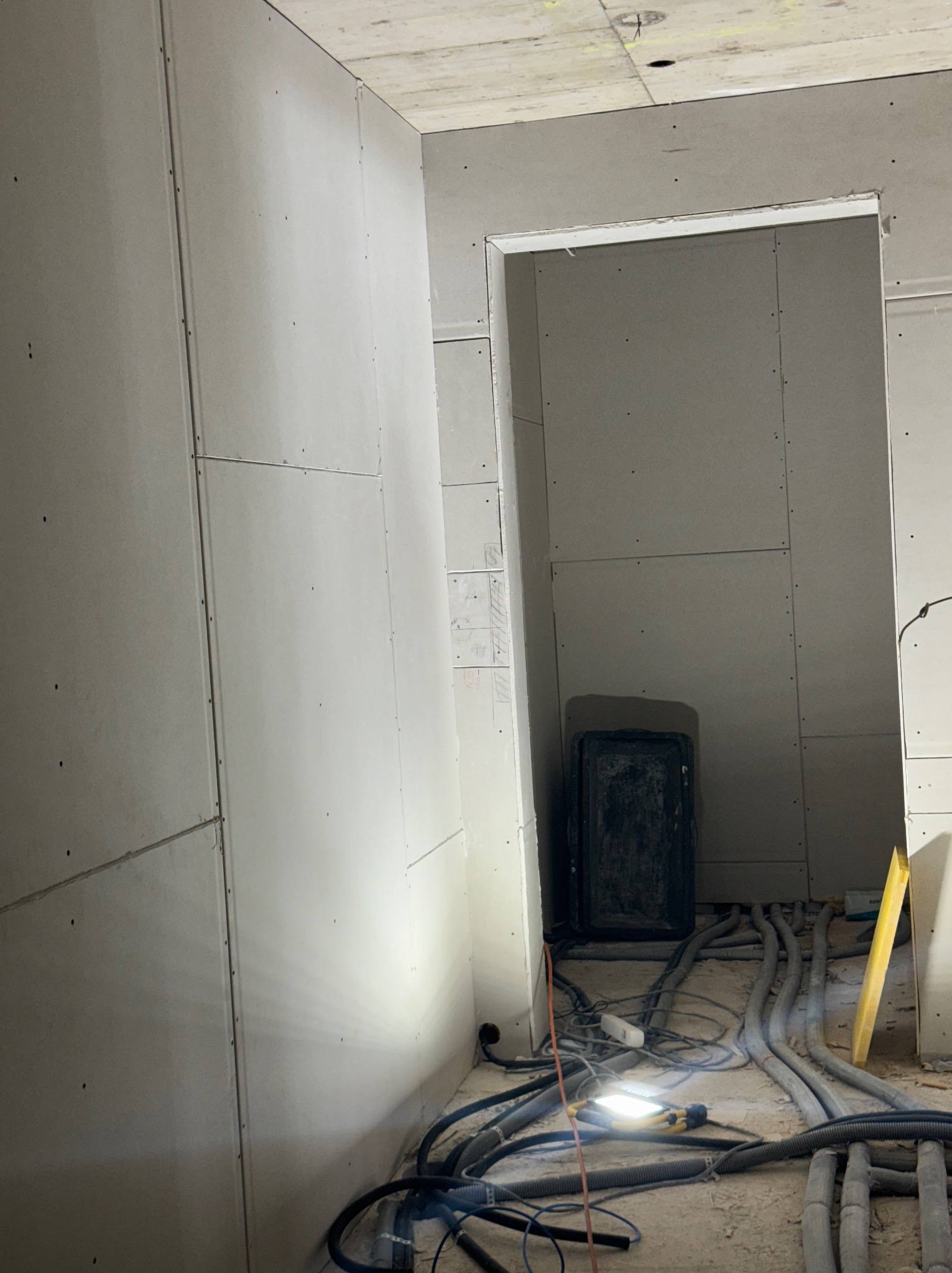 Montaż płyt gipsowo-kartonowych w Radomiu, widoczne kable i narzędzia. Ściany przygotowane do dalszych prac wykończeniowych, surowy stan.