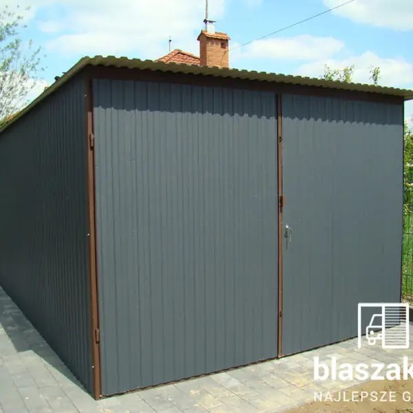 Szary garaż z blachy falistej z brązowymi obramowaniami, widoczny z boku na tle kostki brukowej i zieleni. Na drzwiach widoczne logo producenta.