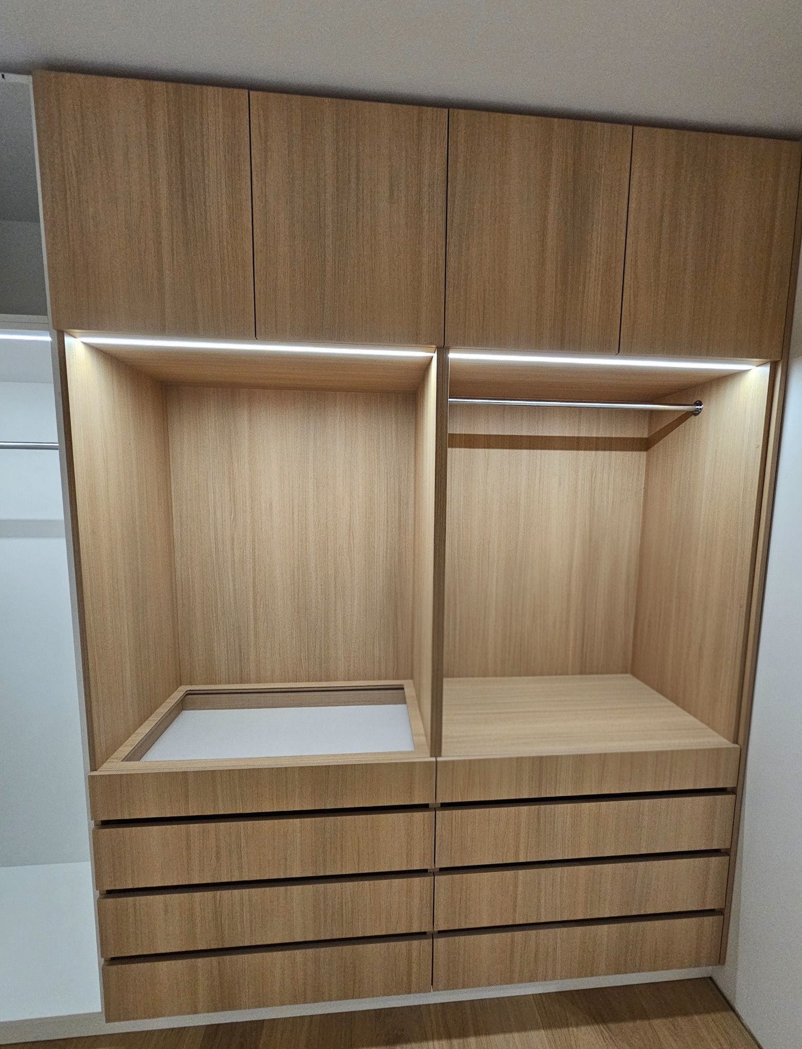 Jasna, drewniana szafa wnękowa z oświetleniem LED, widoczne półki i szuflady. Minimalistyczny design, ciepłe światło podkreśla strukturę drewna.