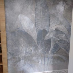 Nowy horyzont - Ściana z motywem liści w odcieniach szarości po odświeżeniu w Świerklańcu. Widoczny fragment podłogi i wiadro z farbą, co sugeruje prace wykończeniowe.