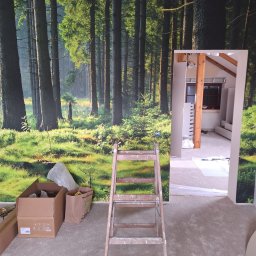 Nowy horyzont - Pokój w trakcie tapetowania fototapetą z motywem leśnym. Widoczna drabina malarska, kartony i otwarte przejście do innego pomieszczenia.