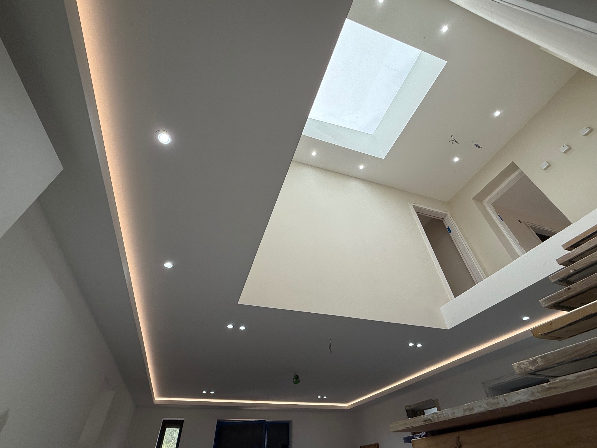 Nowoczesny sufit z oświetleniem LED i świetlikiem, widok z dołu. Jasne, świeżo wykończone wnętrze z elementami w odcieniach bieli i szarości. Widoczne detale wykończeniowe.