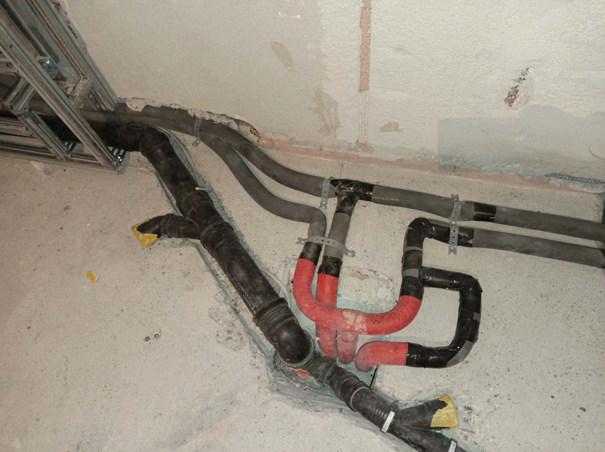 Ułożone rury kanalizacyjne i grzewcze w surowym stanie, z widocznymi mocowaniami i izolacją, przed zakryciem w ścianie lub podłodze. Detal instalacji.