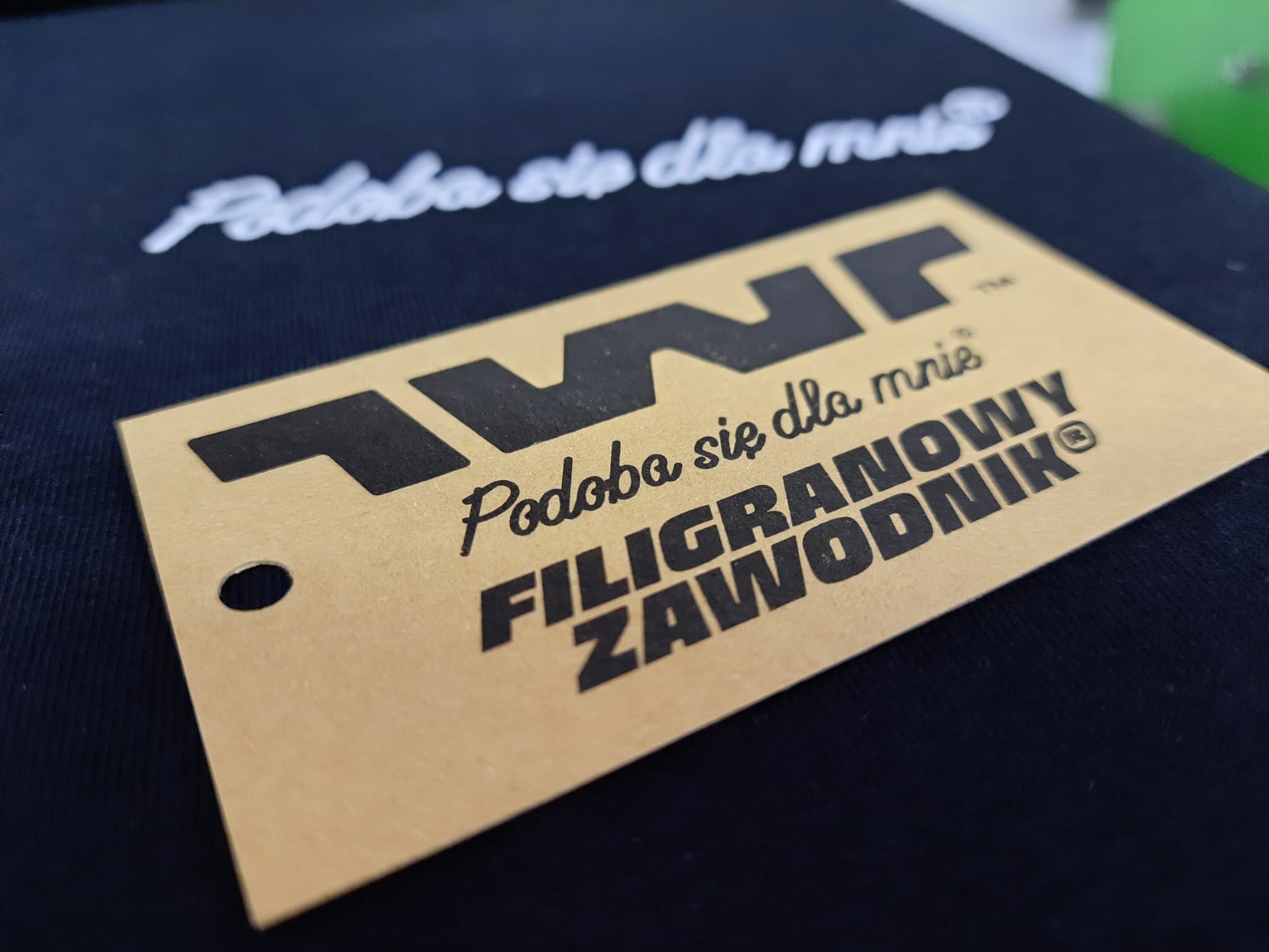 Czarna koszulka z białym napisem i beżową etykietą z czarnym nadrukiem 'Filigranowy Zawodnik'. Detal prezentujący unikalny projekt graficzny na odzieży.