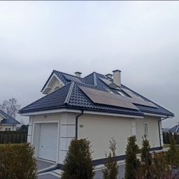 SITARSKY ENERGY SPÓŁKA Z OGRANICZONĄ ODPOWIEDZIALNOŚCIĄ - Dom z panelami słonecznymi na dachu w pochmurny dzień. Widoczne panele fotowoltaiczne na ciemnym dachu, jasna elewacja budynku i zadbany ogród. Ujęcie z dołu.