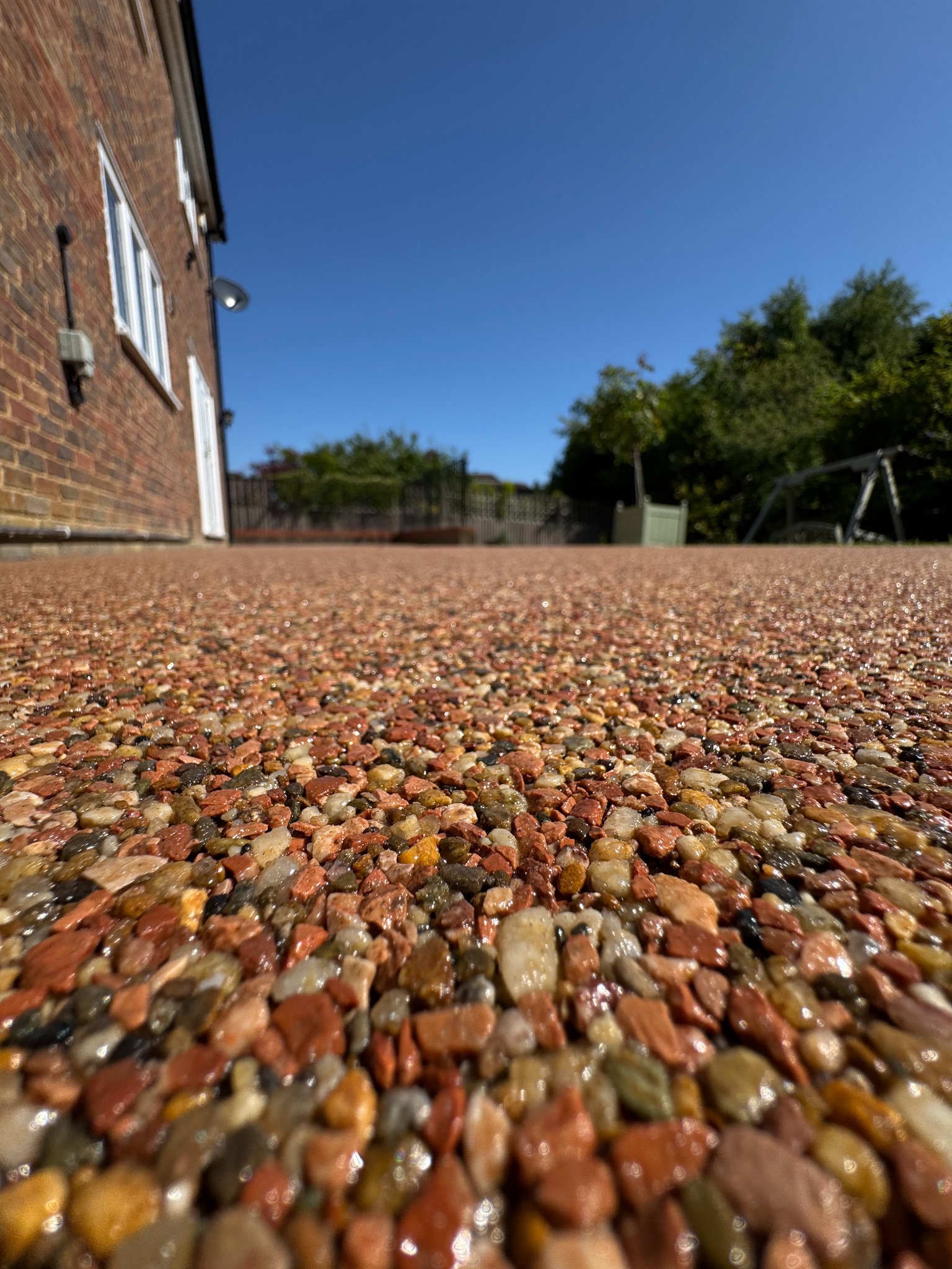 Błyszcząca, kamyczkowa nawierzchnia na zewnątrz domu z cegły, widziana z niskiej perspektywy, podkreślająca fakturę i kolorystykę materiału w słoneczny dzień.