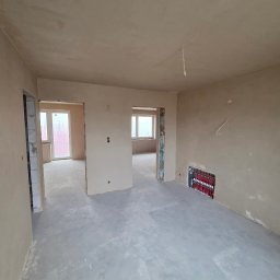 Usługi Ogólnobudowlane Janusz Lewandowski - Wnętrze po tynkowaniu maszynowym: gładkie, jasne ściany i wylewka podłogowa. Widoczna instalacja ogrzewania podłogowego w ścianie. Surowy stan wykończenia.