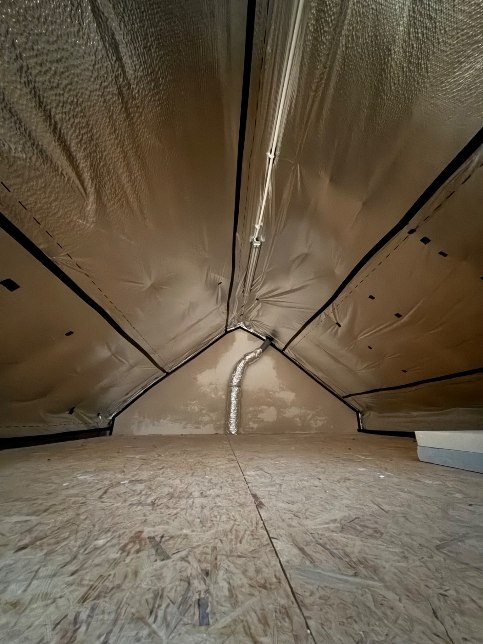 Izolacja poddasza z folią aluminiową i widoczną wentylacją, surowa podłoga z płyty OSB. Ujęcie z dołu, podkreślające geometrię dachu.