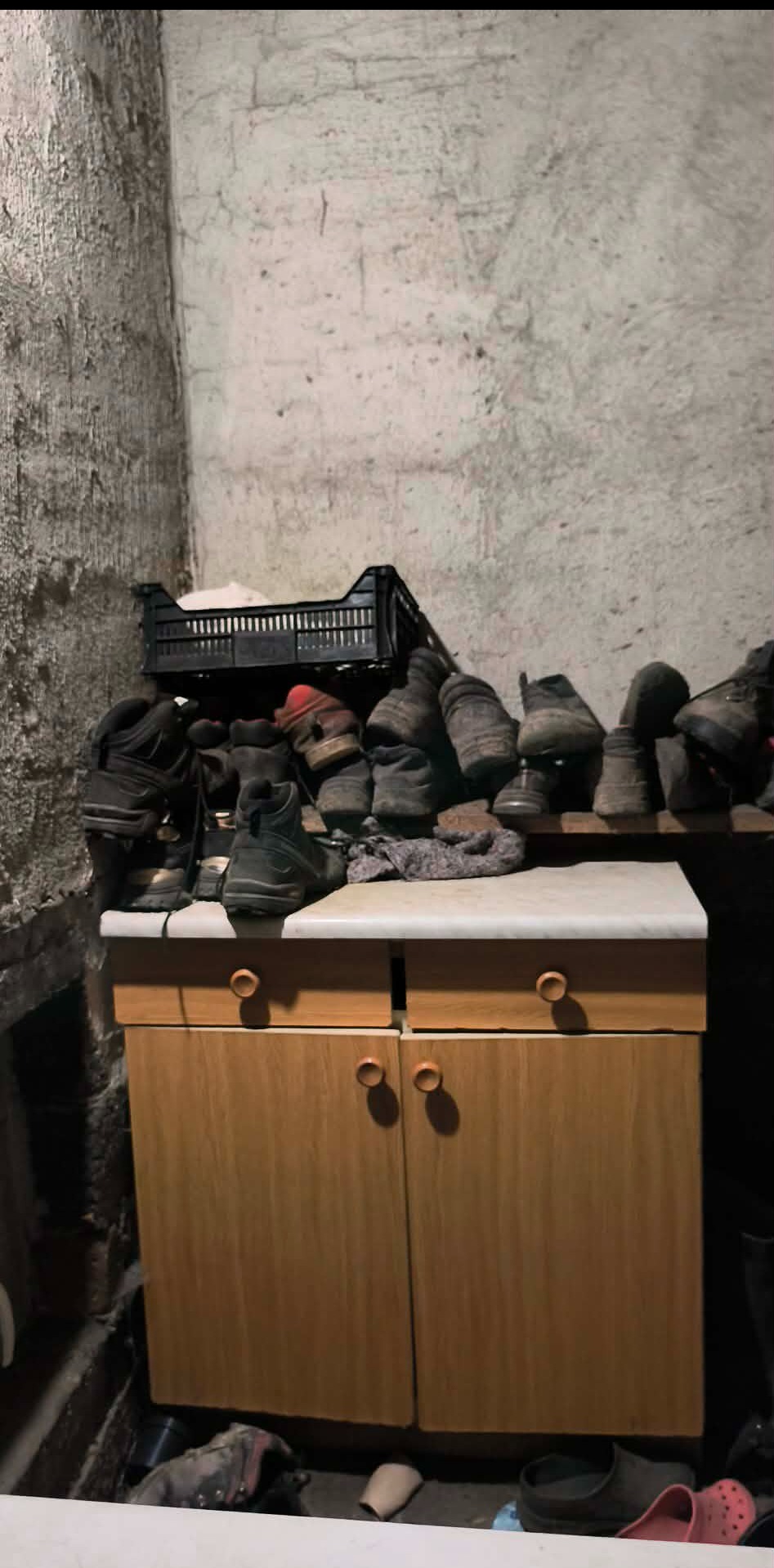 Stare buty ułożone na szafce w zaniedbanym pomieszczeniu. Widoczna skrzynka i ściany z odpadającym tynkiem. Scena sugeruje potrzebę opróżnienia i posprzątania.
