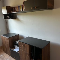 Szymon Szczygieł - Zestaw mebli do salonu z ciemnego drewna i czarnymi blatami, wiszące szafki z książkami, dolne szafki z otwartymi półkami i szufladami, nowoczesny design.