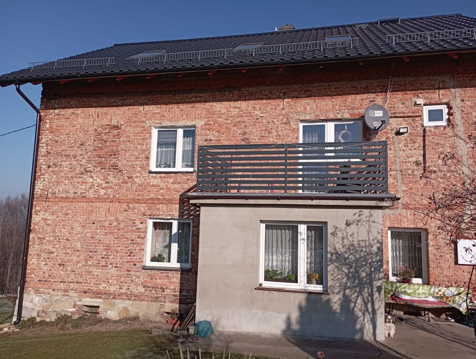 Odnowiona fasada 200-letniego domu z cegły w Pruszkowie. Widoczny balkon z szarą balustradą i okna z białymi ramami. Zachowany historyczny charakter budynku.