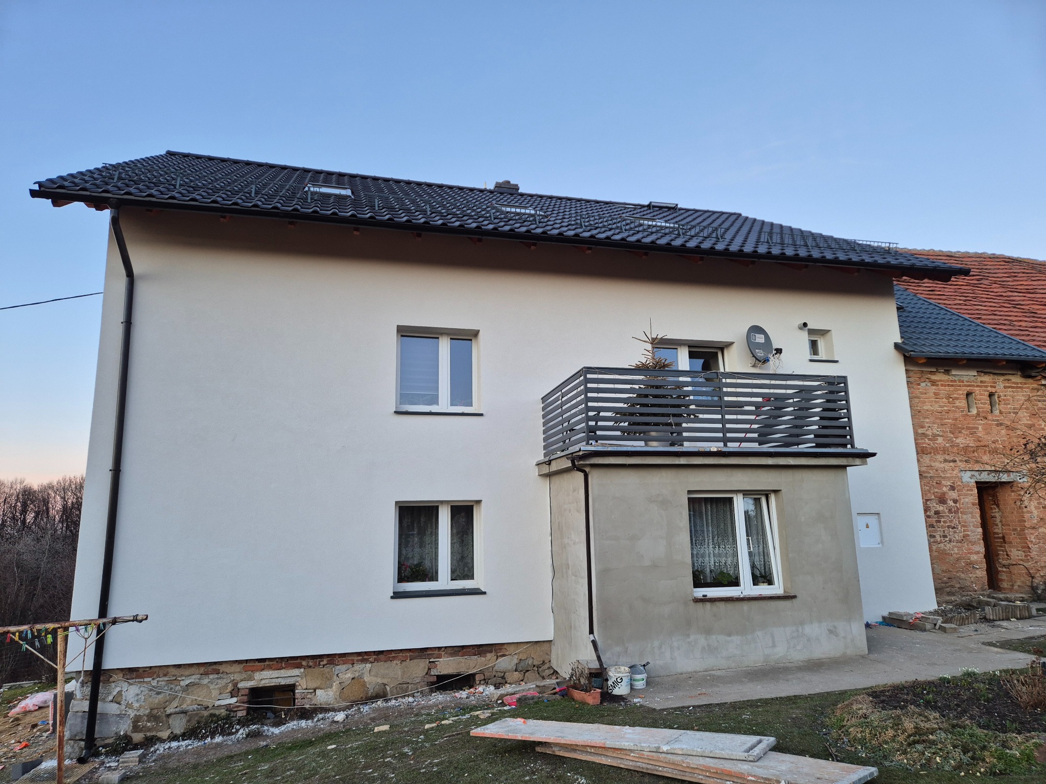 Dwukondygnacyjny dom z balkonem po renowacji elewacji, z nowym tynkiem i pomalowaną fasadą na jasny kolor. Widoczne detale wykończeniowe i otoczenie budynku.