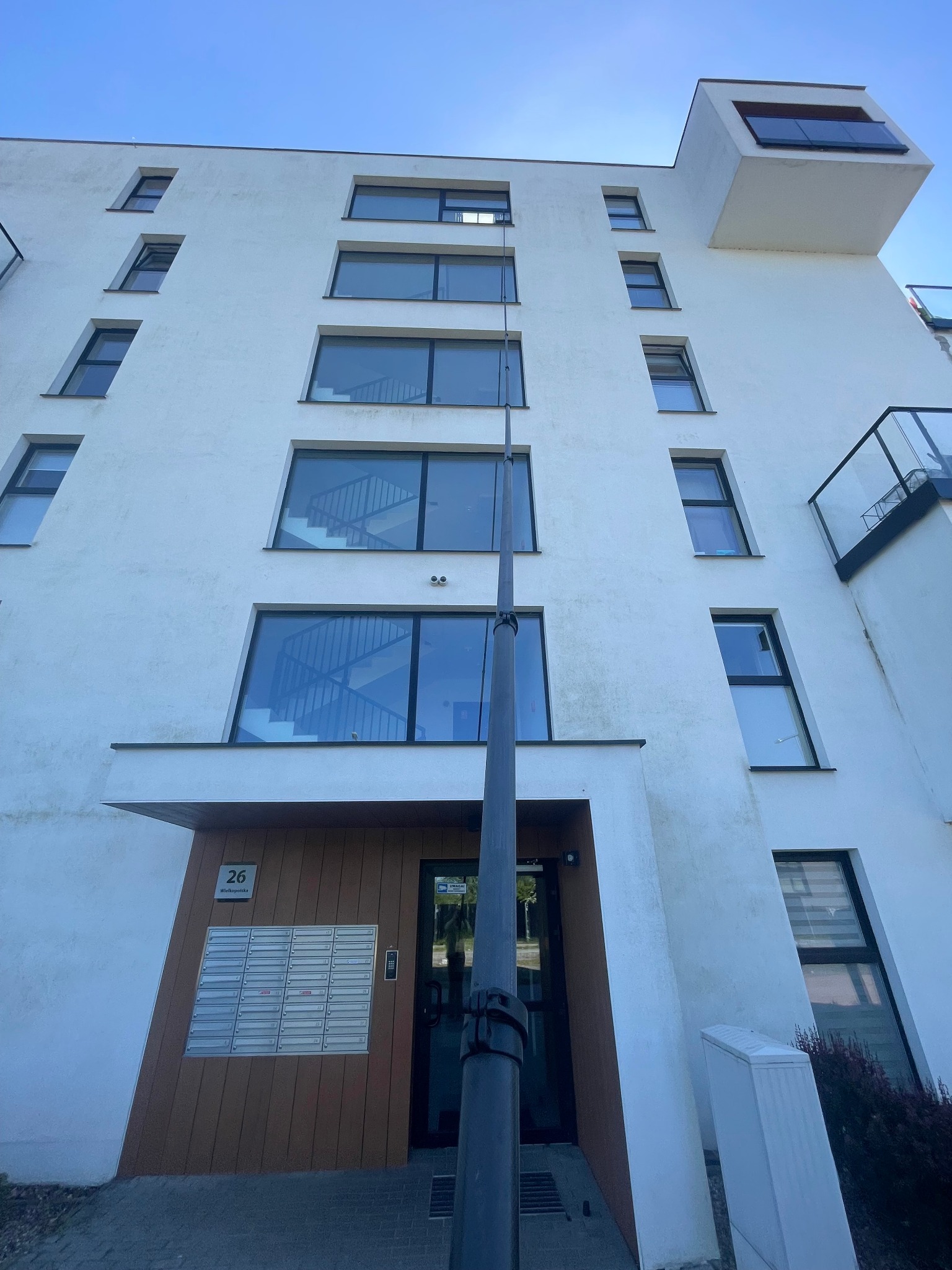 Mycie okien na wysokości w Gdańsku. Widok z dołu na białą elewację budynku z oknami, na tle błękitnego nieba, z użyciem specjalistycznego sprzętu do czyszczenia.