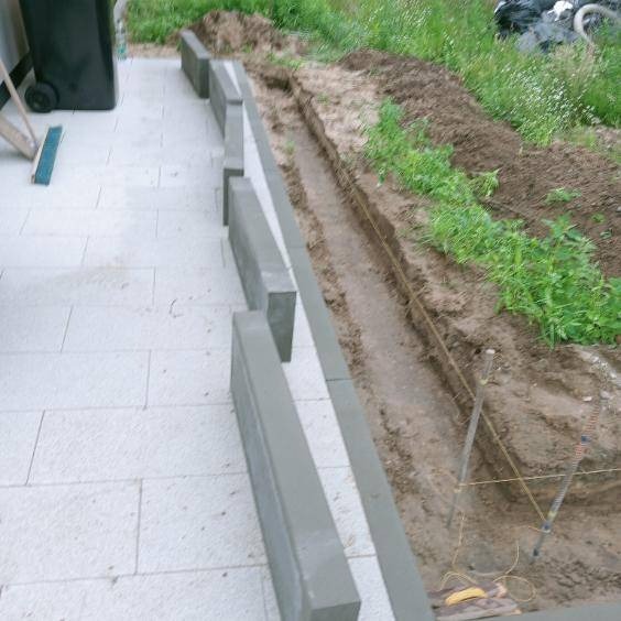 Wykop pod obrzeża kostki brukowej z widocznymi sznurami wyznaczającymi linię, częściowo ułożona kostka brukowa i obrzeża. Widok z góry.