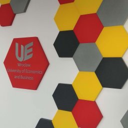 Pro Acoustic Ireneusz Tolak - Dekoracyjne panele akustyczne w kształcie heksagonów w kolorach: czerwonym, żółtym, szarym i czarnym, zamontowane na białej ścianie w biurze Uniwersytetu Ekonomicznego we Wrocławiu.
