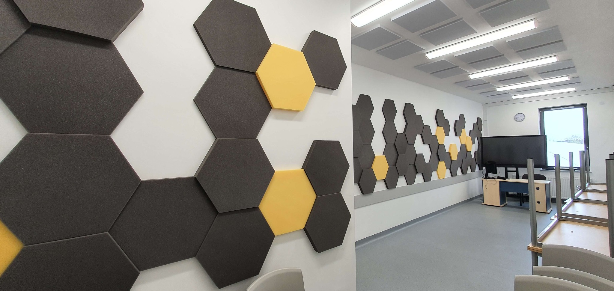 Nowoczesna aranżacja ściany w biurze z heksagonalnych paneli akustycznych w kolorach szarym i żółtym. Widok na salę konferencyjną z panelami na ścianie i suficie.
