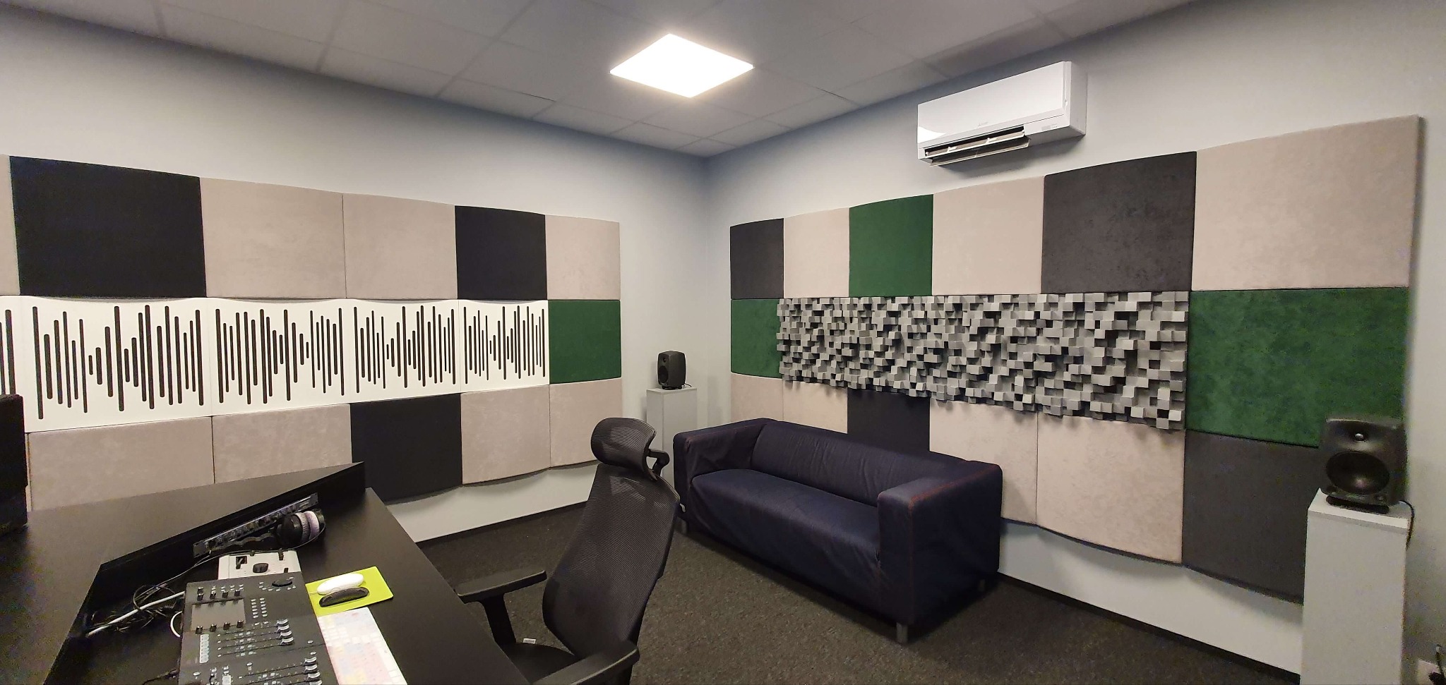 Profesjonalne studio nagrań z panelami akustycznymi w odcieniach szarości, zieleni i beżu. Widoczny sprzęt audio, biurko i sofa. Klimatyzacja na ścianie.