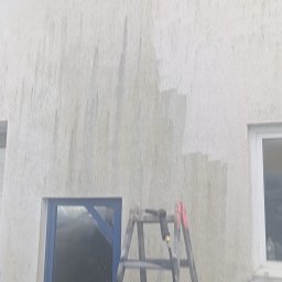Adam Łucyk - Fragment elewacji w trakcie czyszczenia z użyciem drabiny i myjki ciśnieniowej. Widoczne różnice w kolorze, wskazujące na postęp prac.