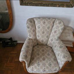 bluestart.kak - Wysokie krzesło tapicerowane w kwiaty, z drewnianymi nogami, stoi na parkiecie. W tle lustro w złotej ramie, gitara i stara maszyna do szycia.