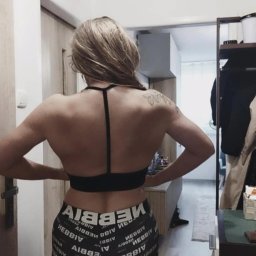 Ewa Iwańska - Kobieta w sportowym stroju, widok z tyłu, prezentująca umięśnione plecy i ramiona. Tatuaż na ramieniu. Ubrana w czarny top i legginsy z napisem.