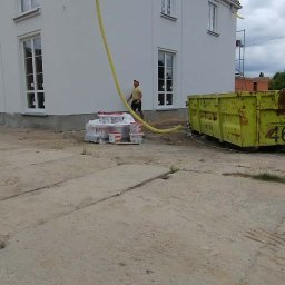 Vasyl Bihun - Biały dom po malowaniu elewacji. Widoczny pracownik z żółtym wężem do agregatu, puszki z farbą i kontener na odpady. Ujęcie z dołu, pochmurne niebo.