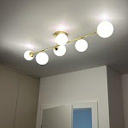 Maciej Nowicki Instalacje Elektryczne - Nowoczesna lampa sufitowa z sześcioma kulistymi kloszami, zamontowana na złotej listwie, oświetlająca wnętrze z białymi ścianami i drzwiami.