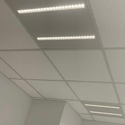 Maciej Nowicki Instalacje Elektryczne - Biały sufit podwieszany z trzema rzędami wbudowanych, prostokątnych lamp LED o ciepłej barwie, oświetlających wnętrze. Widok z dołu, lekki kąt.