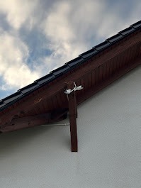 Brązowa drewniana konstrukcja dachu z widocznym kablem elektrycznym przymocowanym do ściany budynku na tle pochmurnego nieba. Ujęcie z dołu.