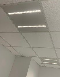 Biały sufit podwieszany z trzema rzędami wbudowanych, prostokątnych lamp LED o ciepłej barwie, oświetlających wnętrze. Widok z dołu, lekki kąt.