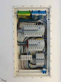 Rozdzielnica elektryczna w białej obudowie, widoczne bezpieczniki, kable i złączki. Uporządkowany układ przewodów, schludne wykonanie instalacji.