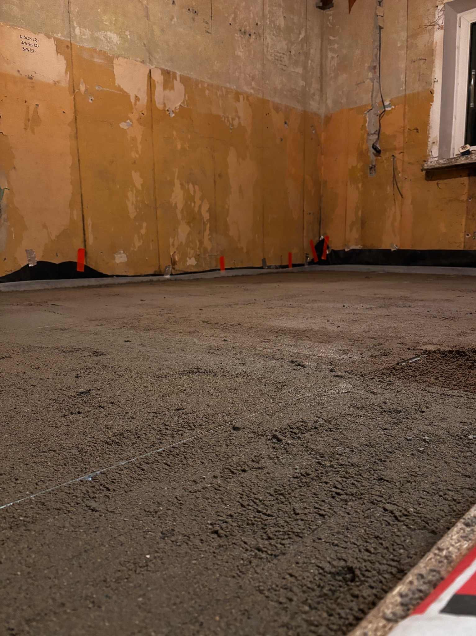 Przygotowanie podłoża pod wylewkę: wyrównany piasek kwarcowy z widocznymi sznurkami poziomującymi, folia izolacyjna przy ścianach z resztkami starej farby.