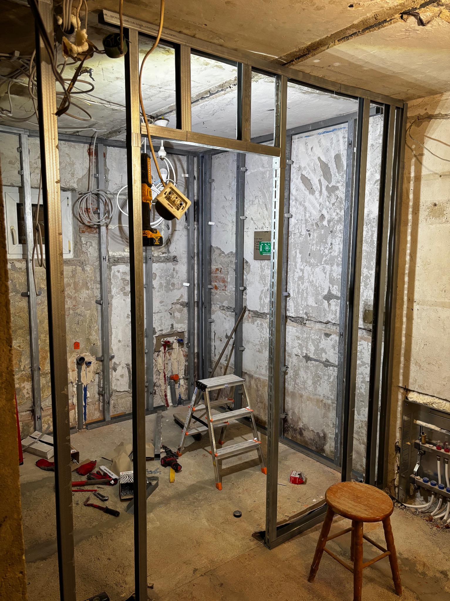 Montaż metalowej konstrukcji ścian działowych w surowym wnętrzu. Widoczne narzędzia, drabina i instalacje. Etap prac wykończeniowych w pomieszczeniu z oknem.