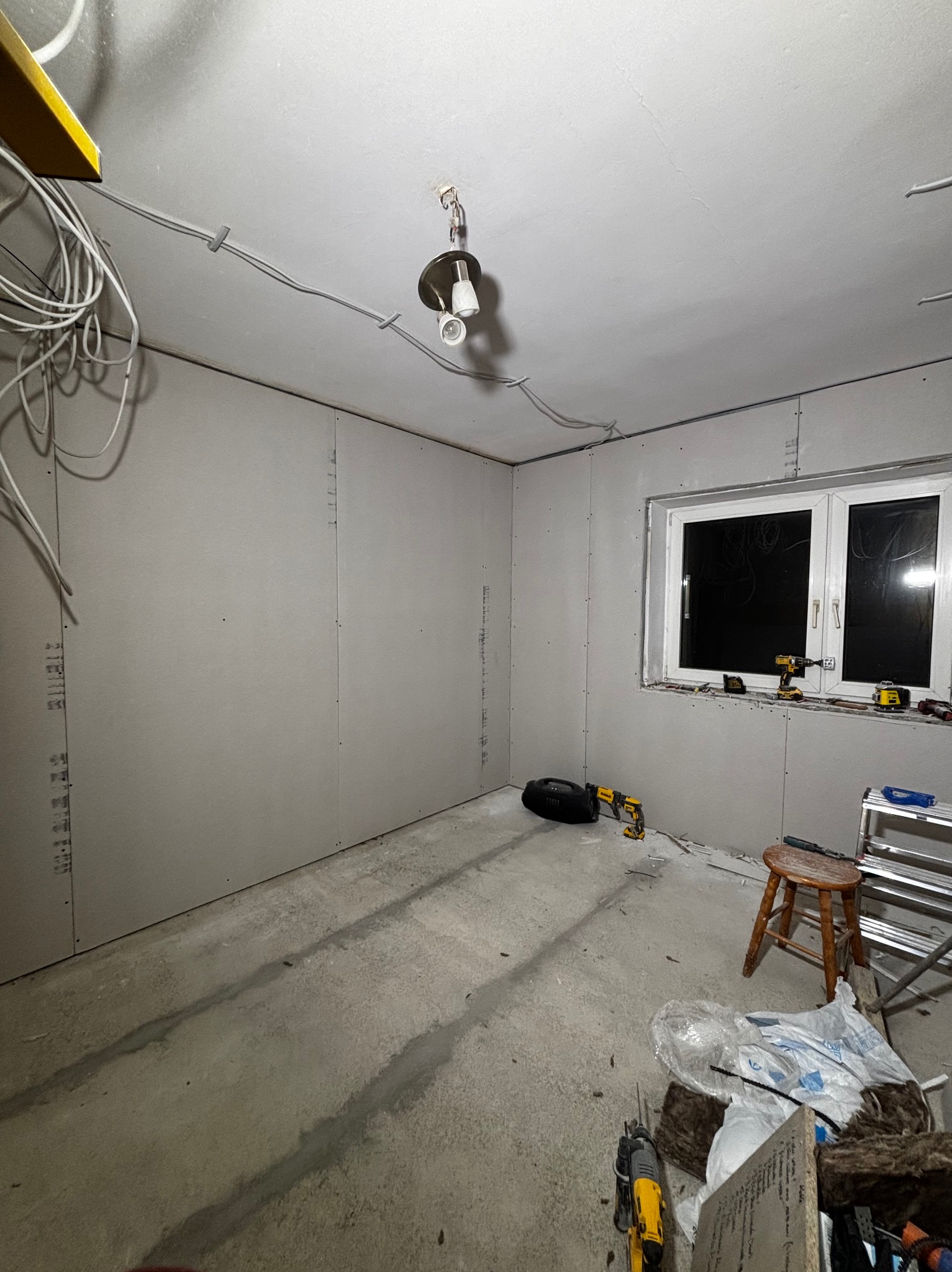 Pokój w Miłoradzu w trakcie montażu płyt gipsowo-kartonowych na ścianach i suficie. Widoczne narzędzia, przewody elektryczne i surowy beton na podłodze.
