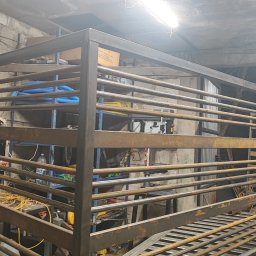 Marcintech - Surowa, metalowa konstrukcja z poziomych prętów w warsztacie, prawdopodobnie fragment bramy lub ogrodzenia, z widocznymi narzędziami i elementami wyposażenia.