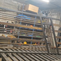 Marcintech - Surowa, metalowa konstrukcja bramy wjazdowej w warsztacie. Widoczne spawy i elementy konstrukcyjne. Tło stanowią narzędzia i materiały warsztatowe.