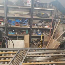 Marcintech - Metalowa konstrukcja w warsztacie, widoczne półki z narzędziami i spawarka. Elementy konstrukcyjne w trakcie tworzenia, surowy wygląd.