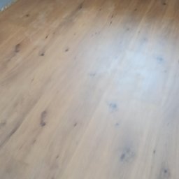 Jacek Sankowski - Ułożone panele podłogowe w pokoju z grzejnikiem i niebieskimi ścianami. Widoczne łączenia paneli i listwy przypodłogowe. Ujęcie z niskiej perspektywy.