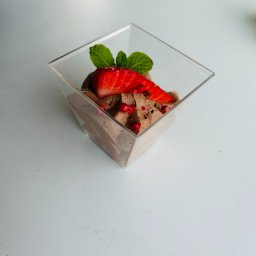 Maincourse.robertpawlina - Deser czekoladowy w przezroczystym kubeczku, udekorowany świeżą truskawką, listkami mięty i różowym pieprzem na białym tle. Elegancka kompozycja.