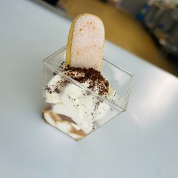 Maincourse.robertpawlina - Deser tiramisu w przezroczystym kubeczku, z biszkoptem savoiardi, kremem i posypką kakaową, na białym tle. Widok z góry, ostre światło.