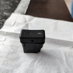 Grzegorz Pawul - Czarny, prostokątny element z widocznymi warstwami, prawdopodobnie wykonany metodą addytywną, leży na białej, teksturowanej powierzchni. Widoczne detale i numery seryjne.