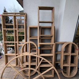 ELASER - Drewniane ramy okienne o różnych kształtach (prostokątne, łukowe) po obróbce, ułożone na zewnątrz budynku. Widoczne detale słojów drewna i delikatne różnice w odcieniach.