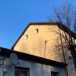 B&L Clean - Dwukondygnacyjny budynek z żółtą elewacją i anteną satelitarną na szarej ścianie, widziany pod kątem z drzewem bez liści po prawej stronie na tle błękitnego nieba.