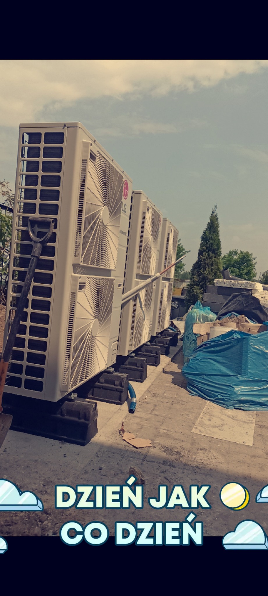 Rząd białych jednostek zewnętrznych klimatyzacji LG, ustawionych na czarnych wspornikach na betonowym podłożu, z łopatą opartą o pierwszą jednostkę. Widok z dołu.